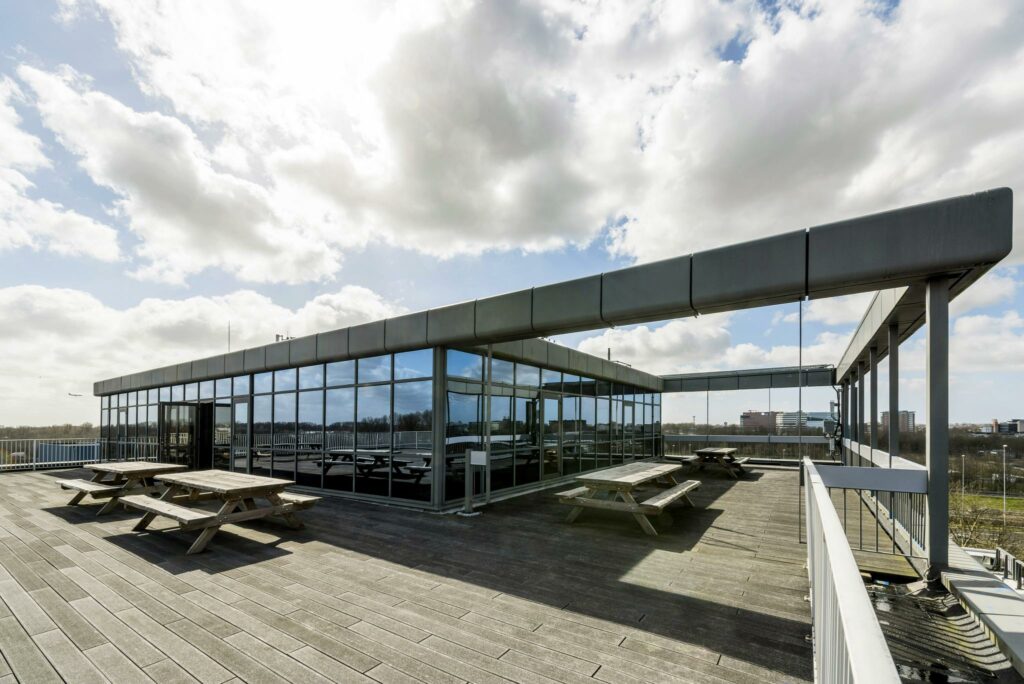 Dakterras met houten picknicktafels en glazen gevel aan de Anthony Fokkerweg.